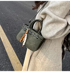 Detail of dark green crossbody bag with woven texture and bohemian bead charm pendant