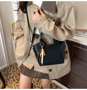 Détail du sac seau en cuir noir avec motif damier et breloque à perles ethnique
