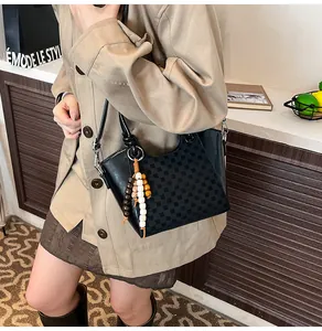 Détail du sac seau en cuir verni noir avec motif à carreaux et pendentif perlé