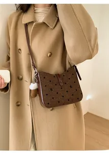 Brown polka dot crossbody bag with bow embroidery and white pompom on beige coat