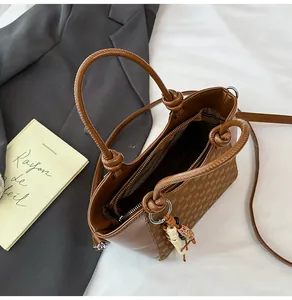 Détail du sac seau marron avec motif à damier, anses rondes et pendentif pompon