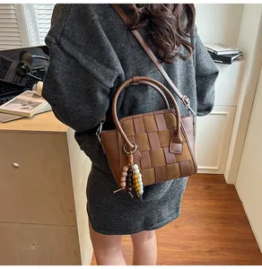 Detail of woven brown leather handbag with wooden bead tassel charm and crossbody strap
