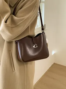 Deep brown leather shoulder bag with silver G-buckle and white fur pompom accessory