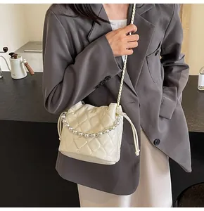 Detail of quilted bucket bag with pearl handle and chain strap on grey blazer