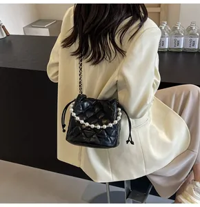 Detail of black quilted bucket bag with pearl handle and chain strap on a model