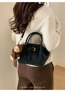 Detail of black suede bucket bag with gold buckle and cute brown teddy bear charm