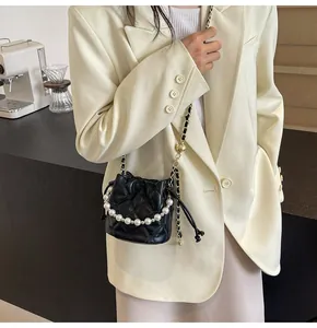 Detail of black quilted bucket bag featuring pearl handle and chain shoulder strap