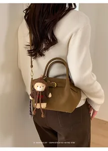 Detail of retro dark brown suede handbag featuring a metal buckle and plush bear charm