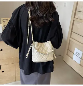 Model view of cream quilted bucket bag with pearl handle and chain strap on shoulder