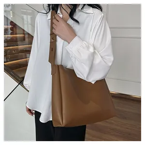 Detail of adjustable wide shoulder strap on brown leather tote bag with metal buckle