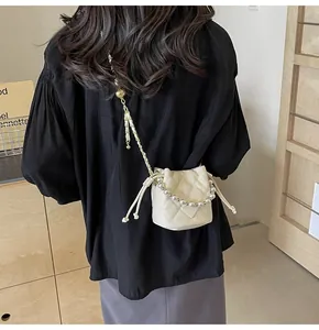 Detail of cream quilted bucket bag featuring pearl handle and gold chain strap