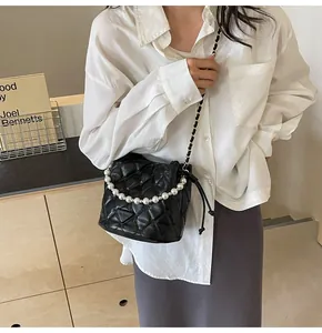 Detail of black quilted bucket bag featuring a pearl handle and metal chain strap
