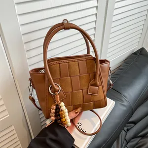 Minimalist woven leather handbag in dark brown finish with beaded charm and top handle
