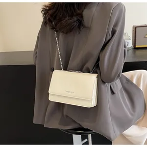 Dettaglio della borsa a tracolla in pelle crema indossata con un blazer grigio elegante