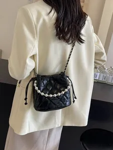 Quilted black bucket bag with pearl handle and chain strap on white blazer