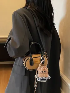 Retro brown leather baguette bag with black handles and plush charm on grey blazer