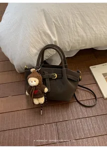 Detail of dark brown suede bucket bag with gold buckle and bear charm on wooden floor