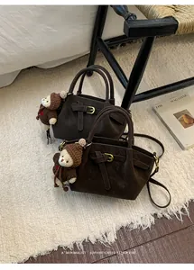 Detail of dark coffee leather handbag featuring matte texture and cute bear charm
