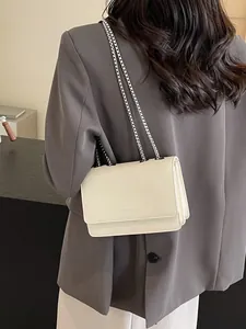 Elegante borsa a tracolla bianco crema con catena da donna su un blazer grigio