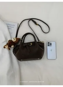 Detail view of mini brown suede bucket bag with a knit bear charm and phone for scale