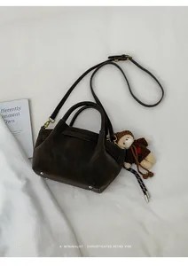 Detail view of coffee brown vintage tote bag with plush bear charm on white fabric