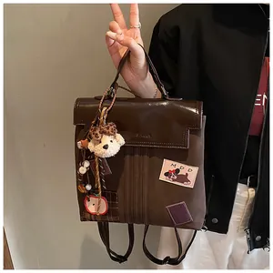 Détail d'un sac à dos bicolore marron avec rabat brillant, patch chien et jolies breloques