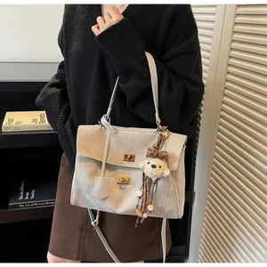 Detalle de bolso tote de ante gris claro con cierres de giro dorados y llavero de peluche