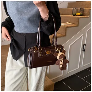 Detalle del bolso baguette marrón café con cierre dorado y colgante de oso de peluche