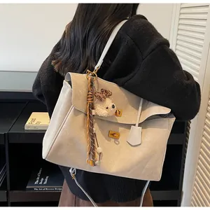 Detalle del bolso tote de ante beige con cierres dorados y colgante de oso de peluche