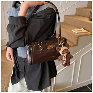 Detalle del bolso baguette de charol marrón oscuro con cierre metálico y un dije de oso
