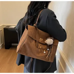 Detalle de bolso tote de ante marrón con cierres giratorios dorados y colgante de peluche