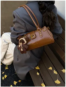 Detalle de bolso baguette de cuero marrón brillante con cierre giratorio y dije de oso