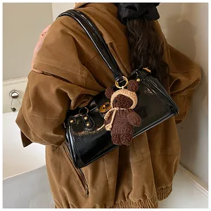 Detalle del bolso baguette de charol negro con un tierno colgante de oso de peluche