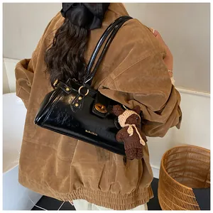Detalle del bolso baguette negro brillante con hebilla dorada y colgante de osito