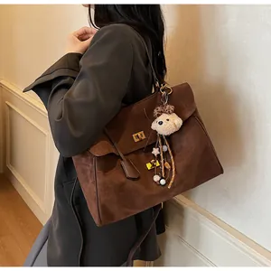 Detalle de bolso tote de ante marrón oscuro con hebilla dorada y amuleto de oso
