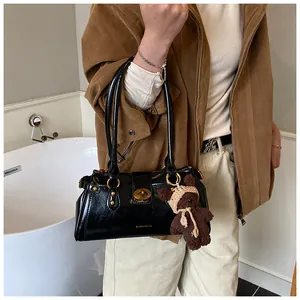 Detalle de bolso baguette de cuero negro brillante con asa larga y colgante de osito