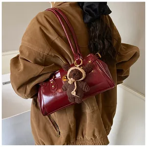 Detalle del bolso baguette de charol burdeos con un tierno colgante de oso tejido