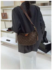 Detail of dark brown monogram hobo bag with wide patterned strap shown on a model
