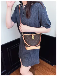 Model wearing a dark brown printed bucket bag with gold lock and thin shoulder strap