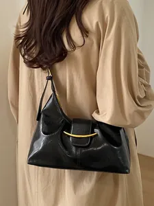 Sac baguette vintage en cuir verni noir avec boucle dorée porté sur un trench-coat