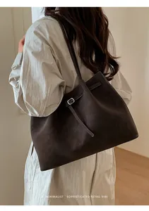 Minimalist coffee brown leather tote bag with silver buckle worn by a model in a cozy room