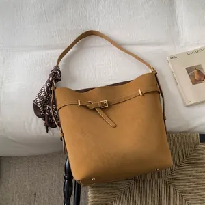 Close-up of brown leather bucket bag with decorative buckle and floral silk scarf detail