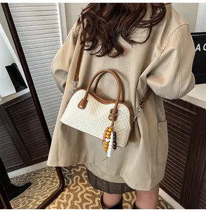 Sac baguette tissé beige avec bordure en cuir marron et gland perlé porté par un mannequin