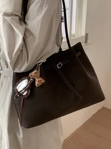 Brown suede tote bag with leopard print bow charm on a model in a beige trench coat