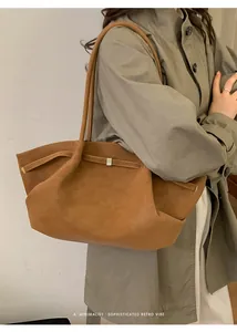 Bolso tote marrón con correas finas y hebillas decorativas sobre un fondo neutro claro