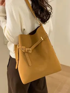 Brown leather bucket tote bag with buckle detail shown on model in a minimalist style