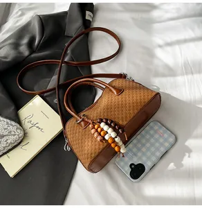 Détail d'un sac Boston tressé marron avec pompon en perles de bois colorées et poignées en cuir