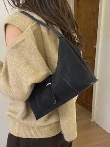 Minimalist black matte leather hobo bag with silver buckle worn by a model in a knit sweater