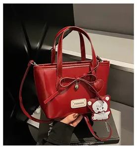 Detail of red glossy bucket bag with bow, metal heart charm and white bear keychain