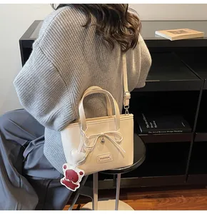 Detailed shot of cream PU bucket bag featuring a bow, bear charm and adjustable strap